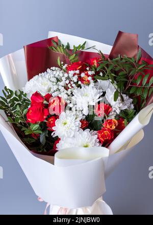 Arrangements floraux. Gros plan de fleurs blanches et rouges enveloppées de papier floral brillant sur fond bleu. Bouquet de roses roses, chrysanthèmes blancs, Banque D'Images