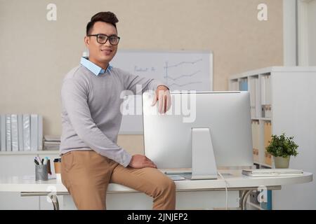 Portrait d'un jeune vietnamien joyeux assis sur le bord de sa table Banque D'Images