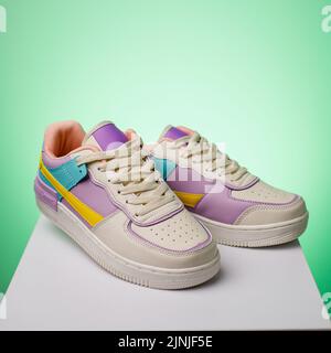 Gros plan sur des sneakers colorées tendance pour adolescentes sur fond vert. Chaussures de sport blanches avec lacets et jaune, turquoise et violet Banque D'Images