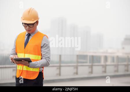 Un jeune responsable de la construction asiatique lit les informations sur une tablette Banque D'Images