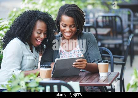Les femmes africaines-Americam sont heureuses et enthousiastes, assis dans un café en plein air et regardant quelque chose sur une tablette numérique Banque D'Images