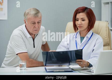 Femme vietnamienne médecin montrant des rayons X des pieds à un patient âgé Banque D'Images