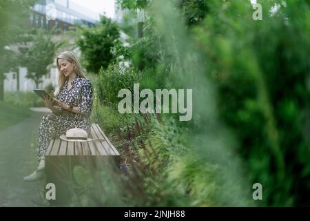 Femme mûre assise sur le banc du parc, appréciant le temps pour elle-même. Banque D'Images