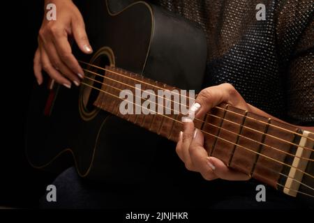 Gros plan d'un musicien méconnaissable portant un chemisier et un Jean jouant de la guitare acoustique, fond noir Banque D'Images