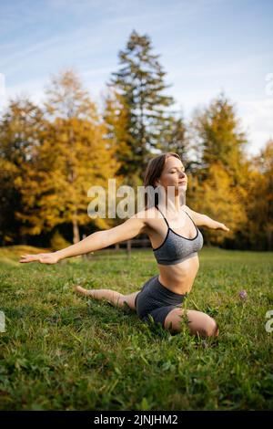 Jeune femme avec un corps flexible dans un haut de sport et short pratique des exercices de yoga sur l'herbe dans les montagnes. Le yoga quotidien aide à façonner le corps Banque D'Images