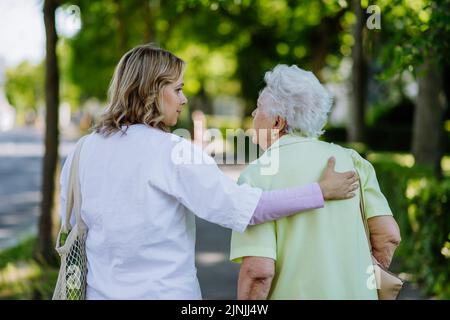 Vue arrière du soignant avec une femme âgée dans un parc avec sac à provisions. Banque D'Images