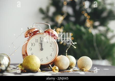 Bonne année ! Horloge rétro élégante, boules de noël scintillantes et lumières dorées sur fond de style moody. Concept de fête du nouvel an. Horloge indiquant minuit. Banque D'Images