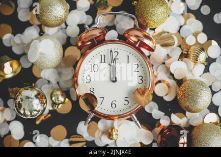 Bonne année ! Horloge rétro élégante, boules de noël scintillantes et confetti dorés à plat sur fond noir. Concept de fête du nouvel an. Horloge affichée Banque D'Images