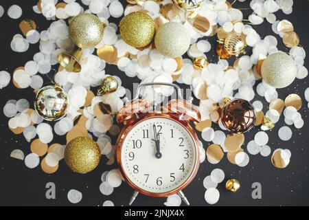 Horloge rétro élégante, boules de noël scintillantes et confetti dorés à plat sur fond noir. Bonne année ! Concept de fête du nouvel an. Horloge affichée Banque D'Images