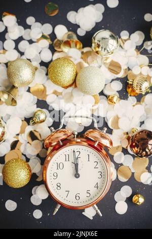 Horloge rétro élégante, boules de noël scintillantes et confetti dorés à plat sur fond noir. Bonne année ! Concept de fête du nouvel an. Horloge affichée Banque D'Images