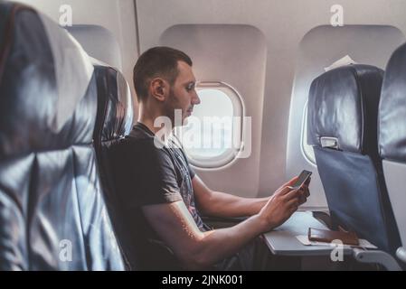 Homme utilisant un smartphone en volant dans un avion Banque D'Images