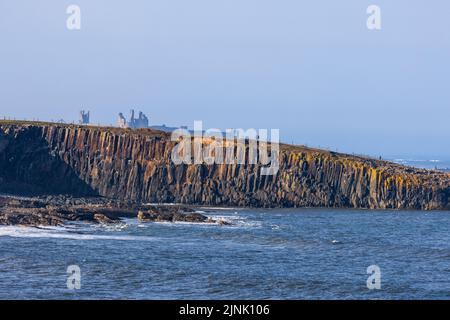 Les roches ignées de Cullernose point sur le chemin de la côte de Northumberland avec le château de Dunstanburgh en arrière-plan, Northumberland, Angleterre Banque D'Images