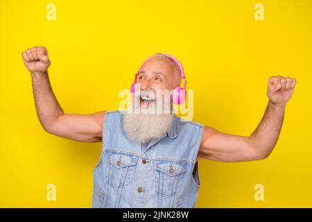 Photo de excitée cool retraité gars porter Jean gilet Ecoute écouteurs regardant l'espace vide isolé couleur jaune arrière-plan Banque D'Images