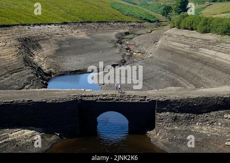 Les gens marchent à travers la terre sèche fissurée au réservoir Baitings à Ripponden, West Yorkshire, où les niveaux d'eau sont considérablement faibles. Le stock total d'eau dans les réservoirs d'Angleterre à la fin du mois de juillet était de 65 pour cent de sa capacité normale - le niveau le plus bas pour ce point de l'année civile depuis 1995, a déclaré l'Agence de l'environnement. Date de la photo: Vendredi 12 août 2022. Banque D'Images