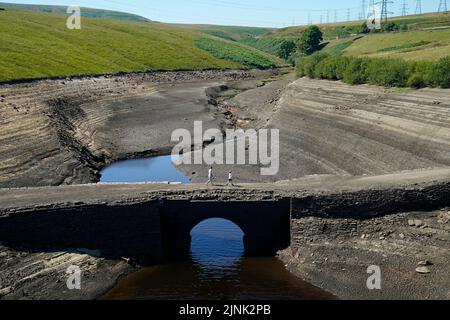 Les gens marchent à travers la terre sèche fissurée au réservoir Baitings à Ripponden, West Yorkshire, où les niveaux d'eau sont considérablement faibles. Le stock total d'eau dans les réservoirs d'Angleterre à la fin du mois de juillet était de 65 pour cent de sa capacité normale - le niveau le plus bas pour ce point de l'année civile depuis 1995, a déclaré l'Agence de l'environnement. Date de la photo: Vendredi 12 août 2022. Banque D'Images