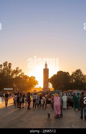Foule de gens sur la place Djemaa El-Fna au coucher du soleil, minaret de la mosquée de Koutoubia en arrière-plan Banque D'Images