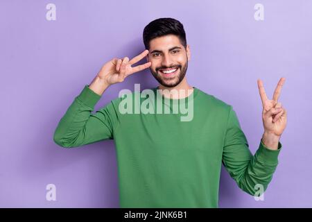 Photo d'une belle personne de bonne humeur vêtue de pull vert montrant le V-signe près de la joue d'oeil isolé souriant sur fond violet de couleur Banque D'Images