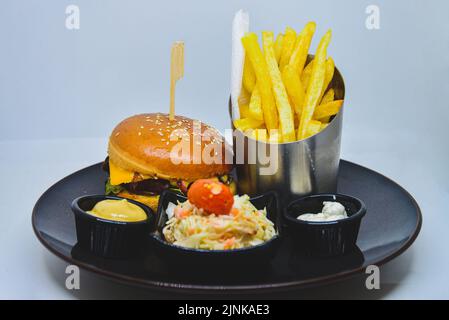 menu de restauration rapide. hamburger, frites et salade. hamburger avec piquet de bœuf, fromage et cornichon. moutarde au ketchup mayonnaise sur l'assiette. Banque D'Images
