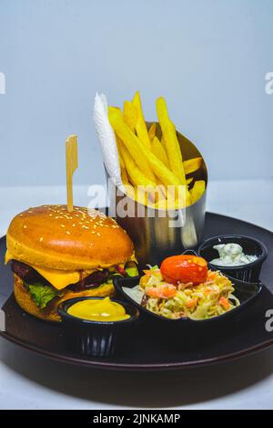 menu de restauration rapide. hamburger, frites et salade. hamburger avec piquet de bœuf, fromage et cornichon. moutarde au ketchup mayonnaise sur l'assiette. Banque D'Images