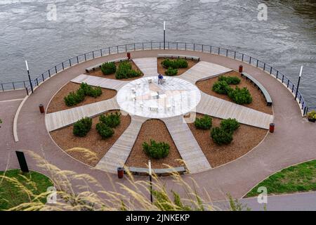 Parc public au bord de la rivière avec plantes décoratives et bancs pour s'asseoir. Banque D'Images