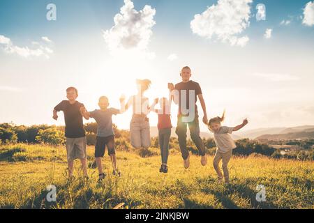 Six enfants frères et sœurs adolescents et petits enfants sautant sur une prairie d'herbe verte avec coucher de soleil en soirée lumière de fond tenant les mains dans les mains et Banque D'Images