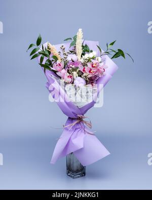 Bouquet d'ingrédients naturels enveloppés de papier à tracer floral dans un vase sur fond bleu. Banque D'Images