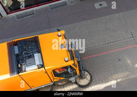 Vue du dessus de la petite machine d'aspirateur à balayage équipement enlever la poussière déchets ville rue trottoir route pavée près de l'immeuble d'appartement Banque D'Images