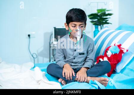 Enfant malade inquiet avec un masque à oxygène assis sur le lit à l'hôpital - concept de problèmes respiratoires, d'infection respiratoire et de traitement de santé. Banque D'Images