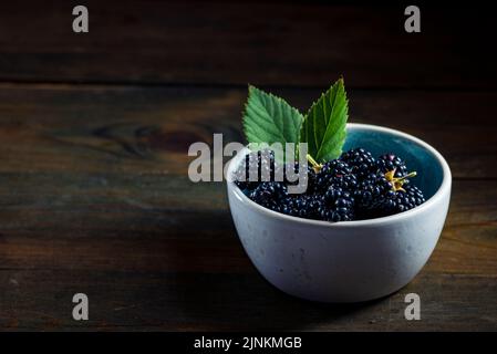 Mûres de mûre avec des feuilles dans un bol d'argile sur un fond de bois sombre photographie de nourriture, Sweet Tasty heap antioxydant bio superfood Banque D'Images