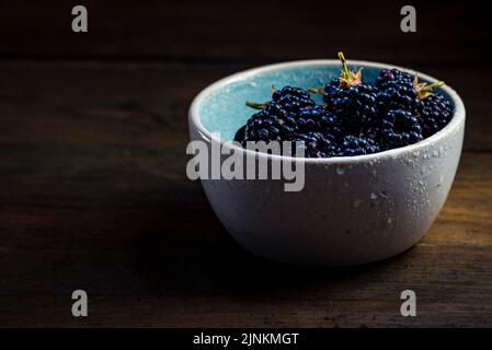 Mûres de mûre avec des feuilles dans un bol d'argile sur un fond de bois sombre photographie de nourriture, Sweet Tasty heap antioxydant bio superfood Banque D'Images