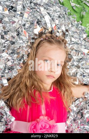 Visage souriant et gai d'une fille dans une robe rose dans une énorme pile de confetti en feuille d'argent, gros plan. Une fille en paillettes étincelantes. Joyeux anniversaire, Banque D'Images