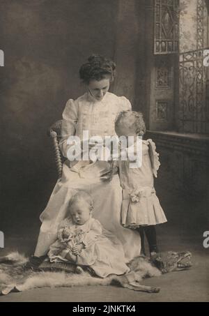 Photographie vintage en noir et blanc de la mère et des enfants dans une posture naturelle de candid pour un portrait de studio d'intérieur époque victorienne vers 1890s Banque D'Images