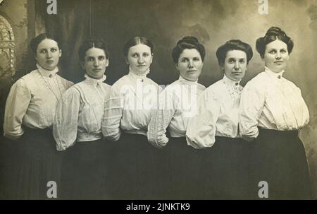 Photographie victorienne en noir et blanc de six jeunes femmes dans une ligne posée pour l'appareil photo avec Gibson Girl coiffant des vêtements d'époque au tournant du siècle vers 1890s à 1900s Banque D'Images