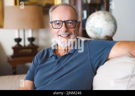 Portrait de tête en gros plan souriant homme retraité plus âgé assis sur un canapé à la maison, grand-père sympathique regardant l'appareil photo, homme mûr à cheveux gris Banque D'Images
