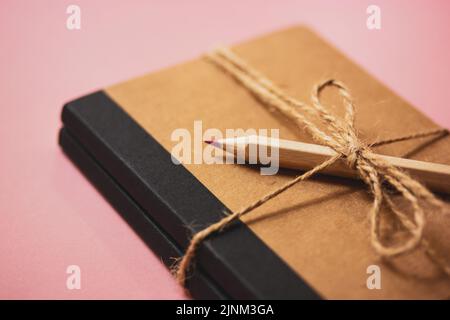 Un carnet de notes écologique pour les notes, attaché avec un noeud en corde. Crayon rose en bois pour les entrées de journal personnelles. Girly, secrets féminins. Accessoires pour Banque D'Images