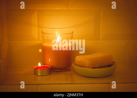 Savon naturel parfumé sur un porte-savon, belle bougie parfumée dans un pot en verre avec une flamme brûlante contre des carreaux décoratifs blancs dans une douche, bathtu Banque D'Images