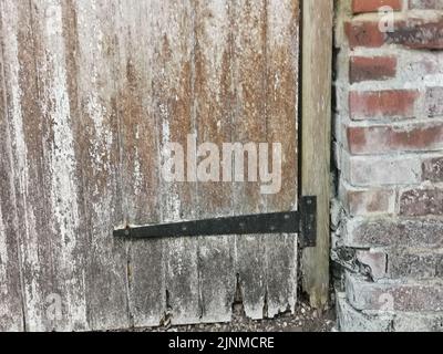 Charnière en métal noir sur l'ancienne porte de rotting avec mur en brique sur le côté Banque D'Images