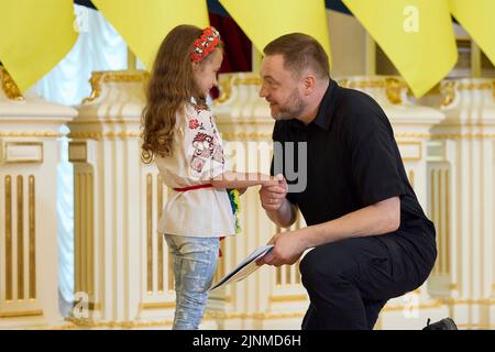 Kiev, Ukraine. 12th août 2022. Denys Monastyrskyi, ministre ukrainien des Affaires intérieures, félicite Irynka Vasilyeva, 7 ans, qui est partie pour célébrer les enfants sauveteurs et les héros de guerre à l'occasion de la Journée internationale de la jeunesse dans la salle blanche des héros du Palais Mariinsky, à 12 août 2022, à Kiev, en Ukraine. Le père d'Irynka a été tué lors de l'invasion russe et elle fabrique maintenant des couronnes de fleurs et les vend pour acheter des armes pour l'armée ukrainienne. Credit: Sarsenov Daniiar/Présidence ukrainienne/Alamy Live News