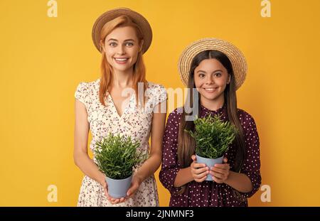 mère et fille sourient avec plante dans pot sur fond jaune Banque D'Images