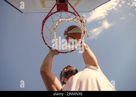 guy dunking ballon de basket-ball à travers anneau de filet avec les mains, gagnant Banque D'Images