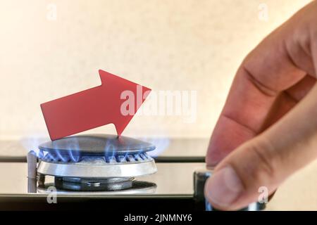 Prix de l'essence. Les chaînes d'approvisionnement et la crise du gaz énergétique. Cuisinière à gaz avec une flamme brûlante et une flèche graphique pointant vers le haut. La main de l'homme règle l'alimentation en gaz Banque D'Images