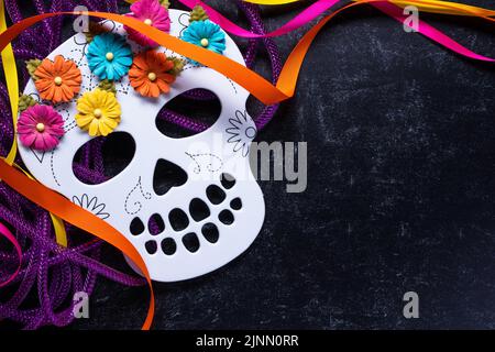 Jour des morts ou Dia de los Muertos fond d'un squelette blanc avec des fleurs rose vif orange, jaune et bleu sur une surface en marbre noir avec m Banque D'Images