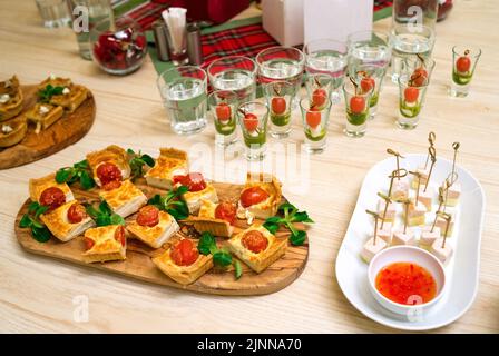 tranches carrées de quiche avec tomates cerises et feuilles de laitue de maïs sur une planche à découper en bois, table de hors-d'œuvre avec en-cas et canapés Banque D'Images