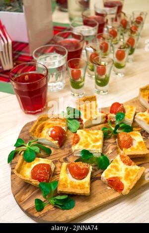 tranches carrées de quiche avec tomates cerises et feuilles de laitue de maïs sur une planche à découper en bois, table de hors-d'œuvre avec en-cas et canapés Banque D'Images