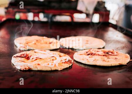 Marionnettes salvadoriennes traditionnelles avec du fromage fondu sur un grill, marionnettes au fromage traditionnel sur le grill. Vue latérale de quatre marionnettes croustillantes traditionnelles Banque D'Images