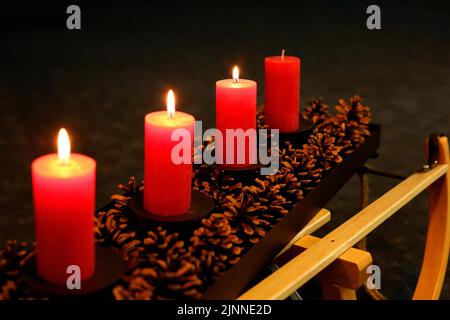 Quatre bougies de l'Avent décorées de cônes de pin sur un traîneau, trois bougies du troisième Avent en feu Banque D'Images