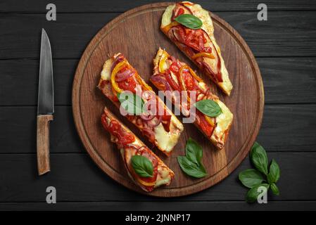 Pain plat de pizza sans gluten. Pizza sur un pain plat avec des légumes sur fond de bois noir. La pizza coupée en tranches repose sur un support en bois. Haut Banque D'Images