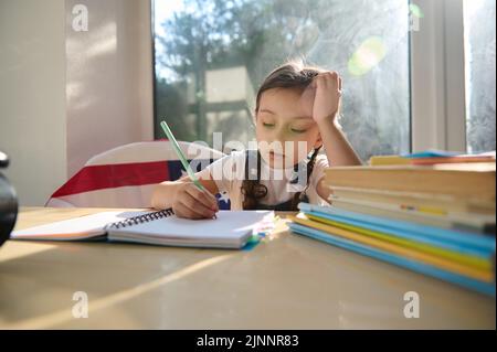 Adorable enfant caucasien écolière apprend à écrire, fait des notes dans son carnet. Retour à l'école. Concept de connaissance Banque D'Images