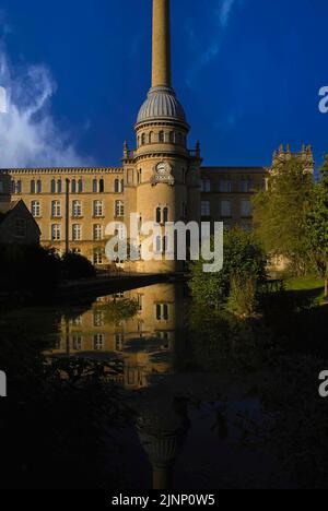 Réflexions sur l'héritage industriel britannique fier à Chipping Norton, Oxfordshire, Angleterre, Royaume-Uni: La façade de style manoir et la tour de cheminée de l'ancien moulin Bliss Tweed, se reflète dans un lac paisible au milieu de jardins paysagers pour les locataires de ses appartements de luxe. La tour porte la date de construction de l’usine en 1872 sous un dôme nervuré et une cheminée qui s’envolait de la fumée de l’eau bouillante du four pour ses machines alimentées à la vapeur. Banque D'Images