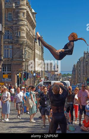 Édimbourg, Écosse, 11 août 2022, Festival Fringe dans le Royal Mile une jeune femme en costume noir qui présente un somersault en plein air Banque D'Images